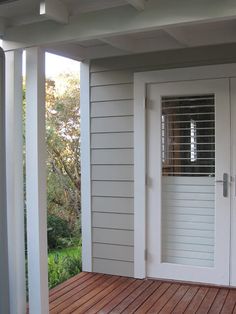 an open door on a porch in front of a white house with wood flooring