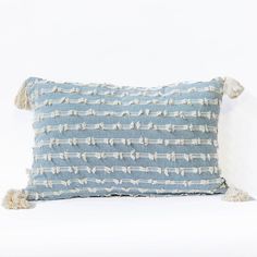 a blue and white striped pillow with tassels on the edges, sitting against a white background