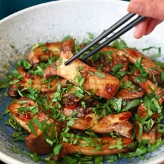 someone is holding chopsticks above a bowl of food with chicken and greens on it