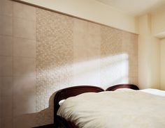 a bed with white sheets and pillows in a bedroom next to a wall that has tiles on it