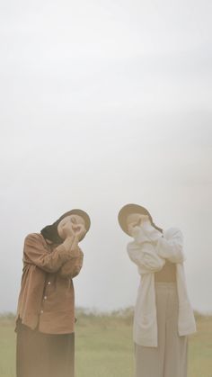 two people standing in the grass with their hands on their hipss and looking up into the sky