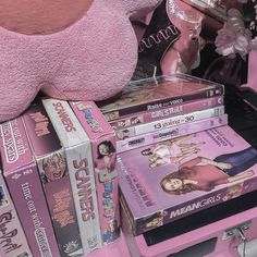 a pink teddy bear sitting on top of a pile of dvd's and dvds