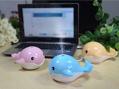 three little whales sitting in front of a laptop on a desk next to some flowers