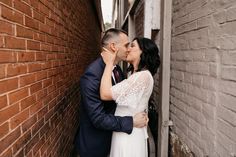 a bride and groom kissing in front of a brick wall on their wedding day at an alleyway