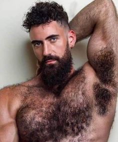 a man with a beard and no shirt is posing for the camera while holding his hands behind his head