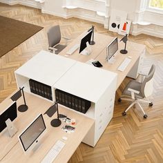 an office cubicle with two desks and three computer screens on it, in the middle of a wood floored room