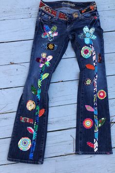 a pair of jeans with colorful patches and flowers on them sitting on top of a wooden floor