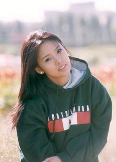 a young woman sitting on the ground with her hands behind her back and looking at the camera