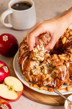 a person is grabbing a piece of apple cinnamon bundt cake from a plate with apples and coffee in the background