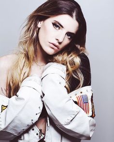 a woman with long hair and an american flag on her jacket is posing for the camera