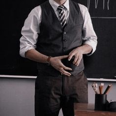 a man standing in front of a blackboard wearing a suit and tie with his hands on his hips