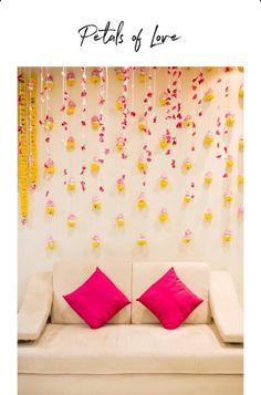 a white couch with pink pillows in front of a floral wall hanging from the ceiling