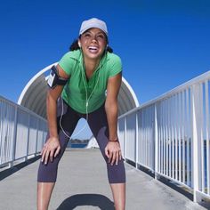 a woman in green shirt and leggings standing on bridge with headphones around her neck