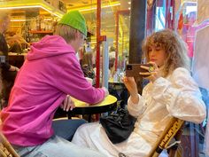 a man sitting in a chair next to a woman who is holding a cell phone