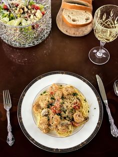 a plate of pasta with shrimp, bread and salad on a table next to wine glasses