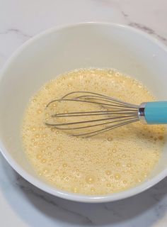 a whisk in a white bowl filled with liquid on top of a marble counter