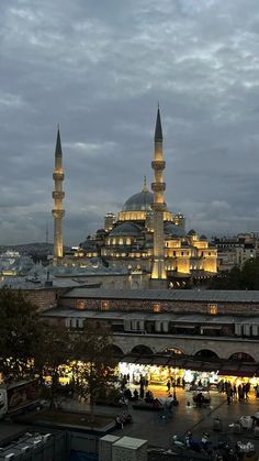 a large building with many lights on it's sides and some buildings in the background