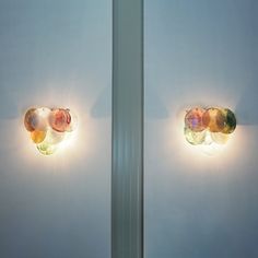 two lights that are next to each other on the side of a wall in front of a mirror