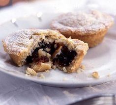 two pastries on a white plate with powdered sugar and crumbled toppings