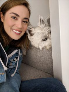 a woman sitting on the floor next to a small white dog and smiling at the camera