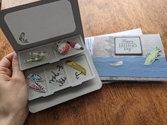 a person holding an open box with pins in it on top of a wooden table