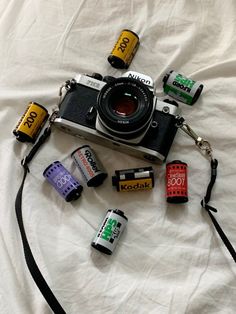 a camera and some batteries are laying on a white sheet with a black strap around it