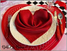 a heart - shaped napkin sits on top of a red and white plate with silverware