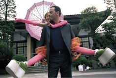 a man and woman dressed up in costumes with pink umbrellas on their heads, holding two large white buckets