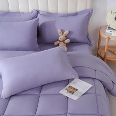 a stuffed animal sitting on top of a purple comforter in a bedroom next to pillows