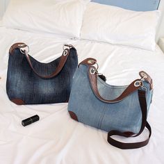 two denim purses sitting on top of a bed