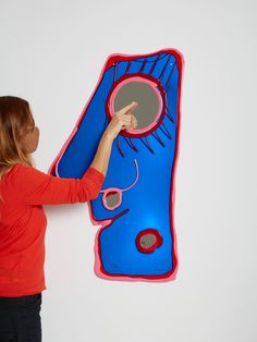 a woman pointing at a blue and red piece of art on the wall with her finger