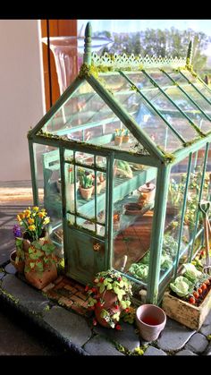 a small green house sitting on top of a stone slab with potted plants in it