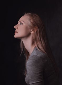 a woman with long hair standing in front of a black background wearing a grey shirt