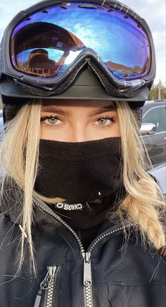 a woman wearing ski goggles and a black jacket with her face covered by a scarf