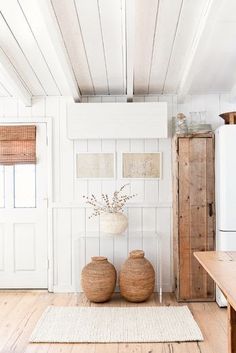 two vases sitting on top of a wooden floor next to a white refrigerator freezer