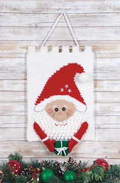 a crocheted christmas ornament hanging on a wall next to evergreen branches