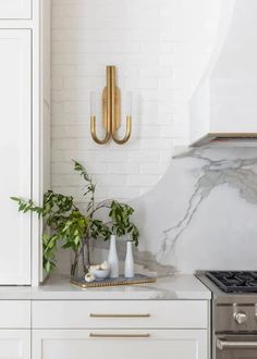 a white kitchen with gold accents and marble counter tops is pictured in this image, there are two vases on the stove