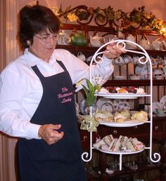 a woman in an apron standing next to a cake stand