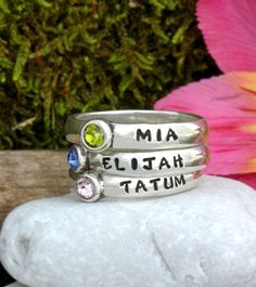 three stack rings with names on them sitting on top of a rock next to flowers