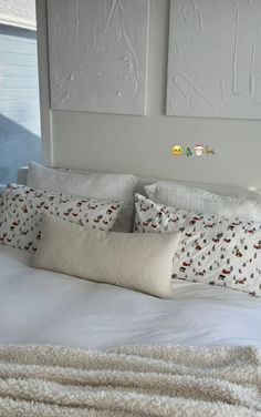 a white bed topped with lots of pillows next to two pictures on the wall above it