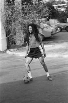 a man with dreadlocks is playing soccer on the street in black and white