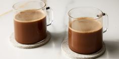 two mugs filled with liquid sitting on top of a marble coaster next to each other