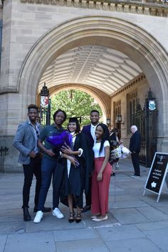 four people posing for a photo in front of an arch with a sign on it