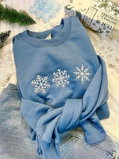 a blue sweatshirt with snowflakes on it sitting next to some jeans and christmas decorations