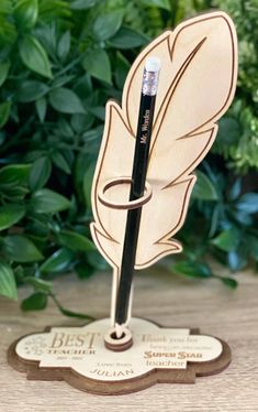 a wooden pen holder with a feather on it and the words best in front of green leaves