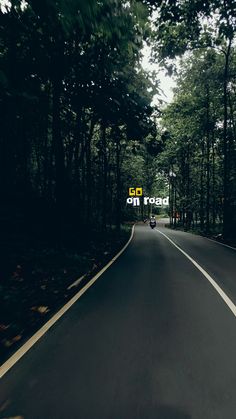 a person riding a motorcycle down the middle of a road with trees in the background