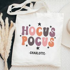 a white tote bag with hoccus pocuss on it next to a hat