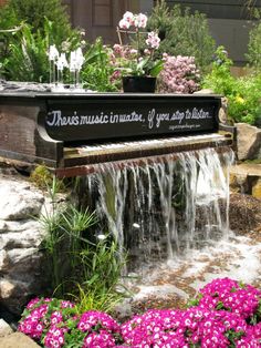 there is a piano in the garden with flowers and water running down it's side