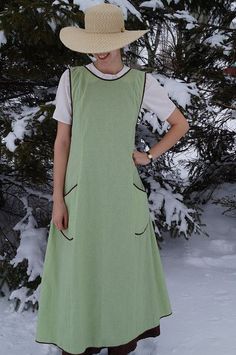 a woman standing in the snow wearing a green dress and hat with her hands on her hips