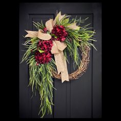 a wreath with red flowers and greenery hanging on a door